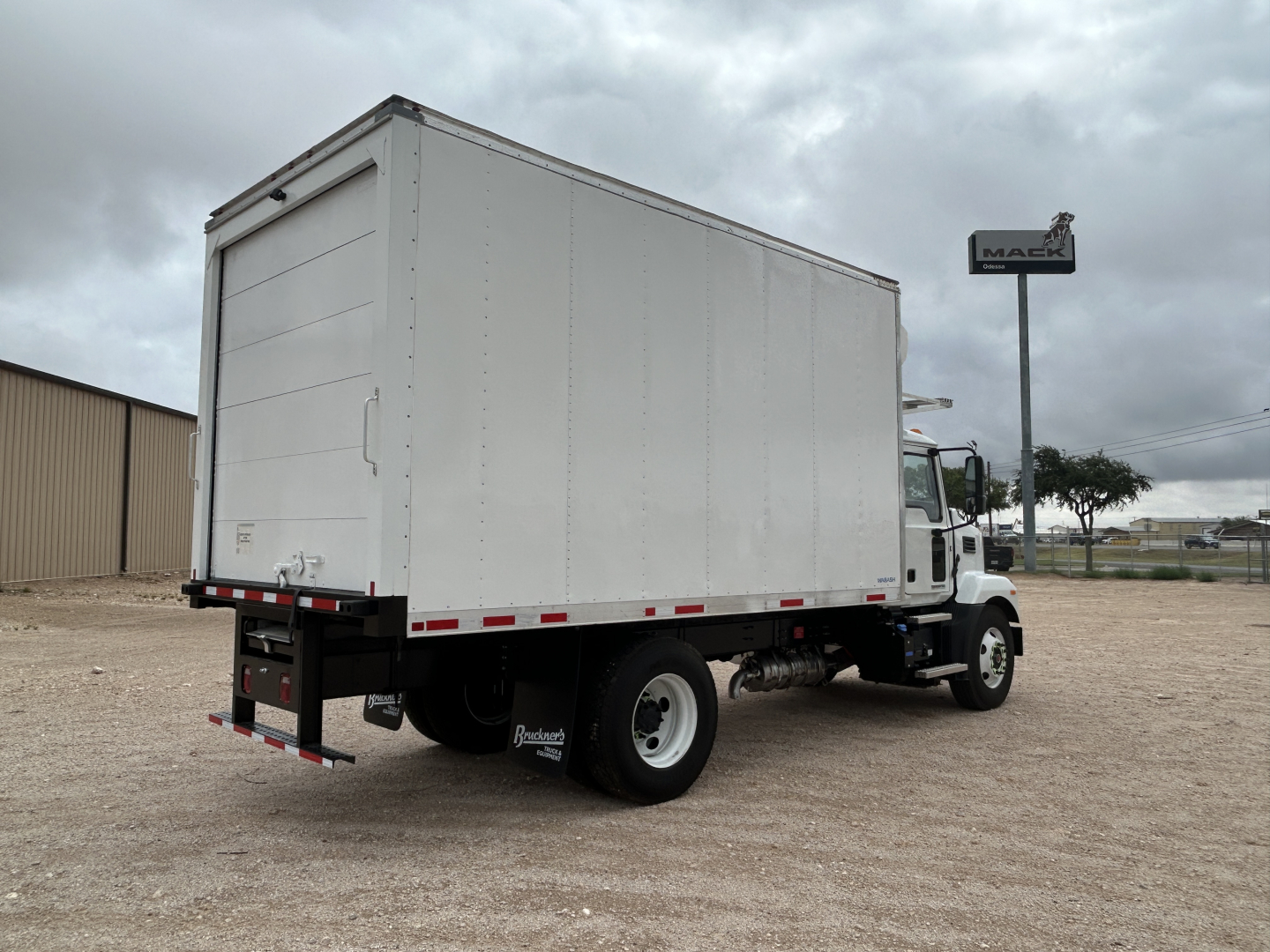 Truck rear and side view showing a white refrigerated box on a Mack MD6 chassis with modest cloud sky.