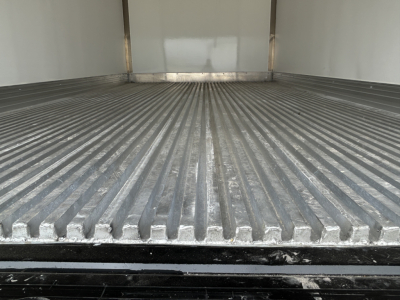 Truck cargo area with ribbed aluminum floor in a refrigerated MD6 trailer showing interior walls and door sill.