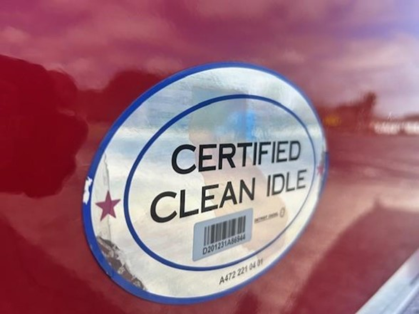 Certified Clean Idle badge on red truck door with barcode and holographic sticker.