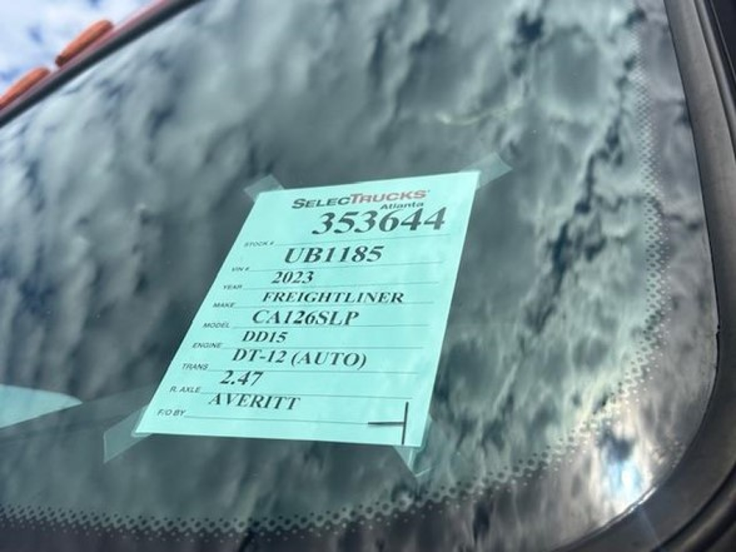 Sticker on windshield with stock number 353644, VIN 3AKJHHDR1PSUB1185, 2023 Freightliner, model DD15 engine, DT-12 auto transmission, 2.47 axle, in-service label.