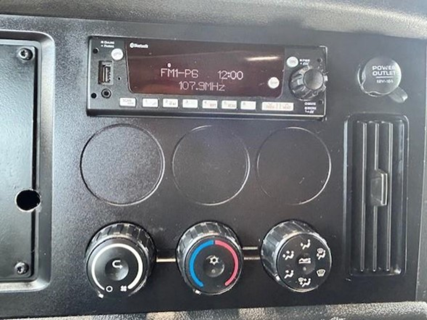 Dash panel of a Freightliner Cascadia showing radio head unit FM1-P6 12:00, climate control knobs, and power outlet. 