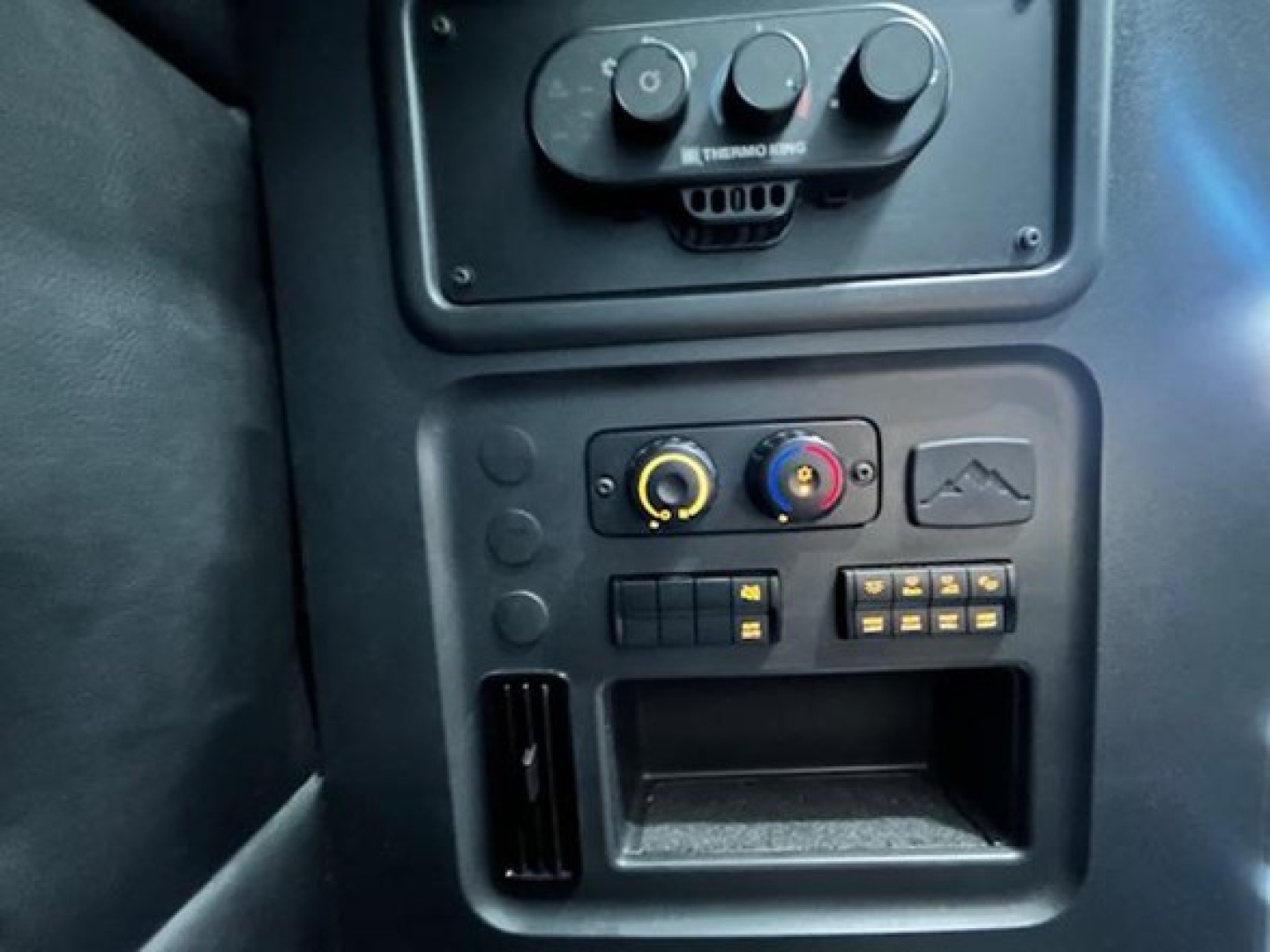 Dashboard controls and climate dials in a Freightliner Cascadia sleeper cab showing circular knobs and a small storage slot.