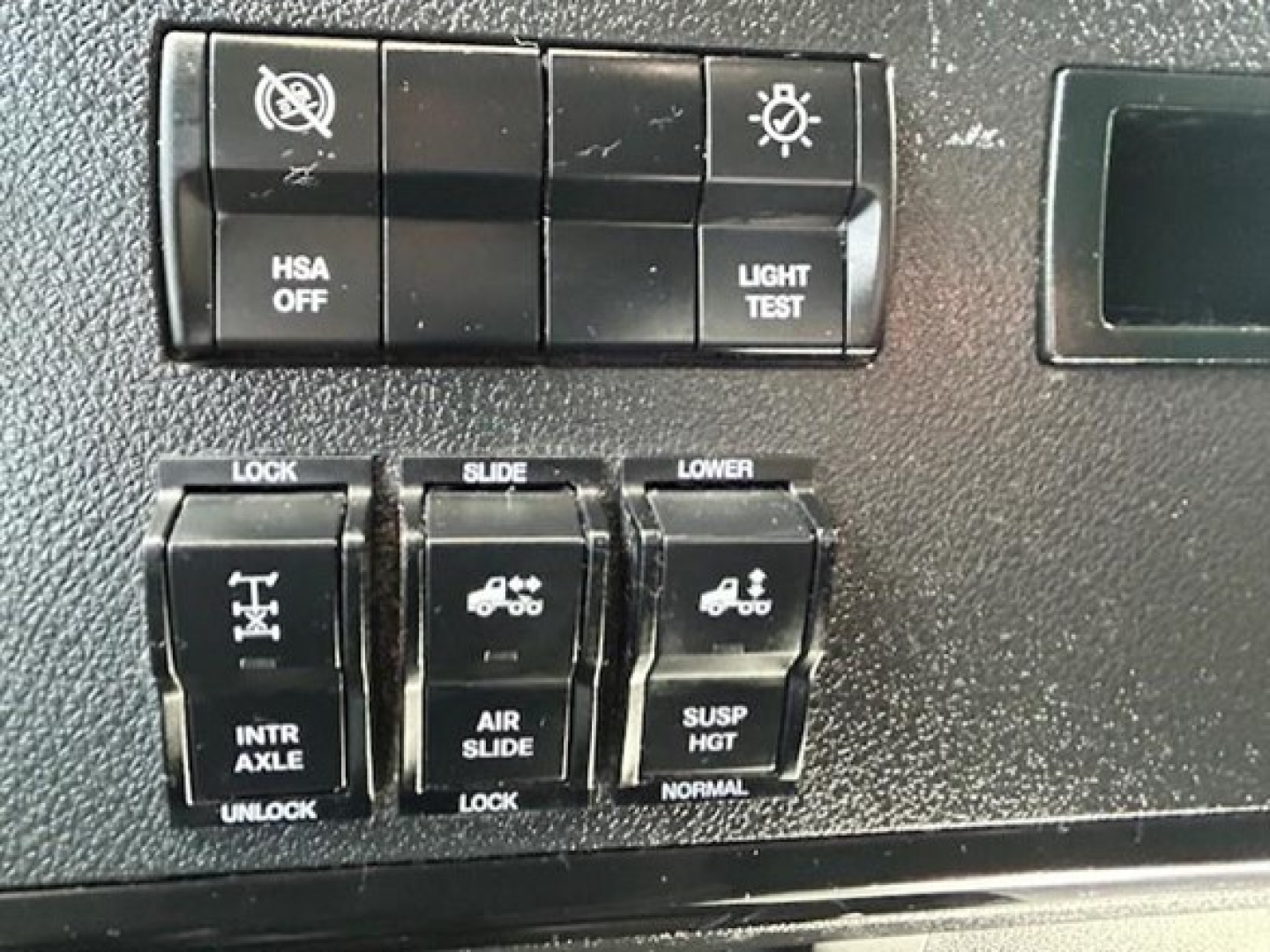 Dashboard switches showing HSA OFF, light test, lock/slide controls and air suspension indicators inside a Freightliner Cascadia truck cabin.