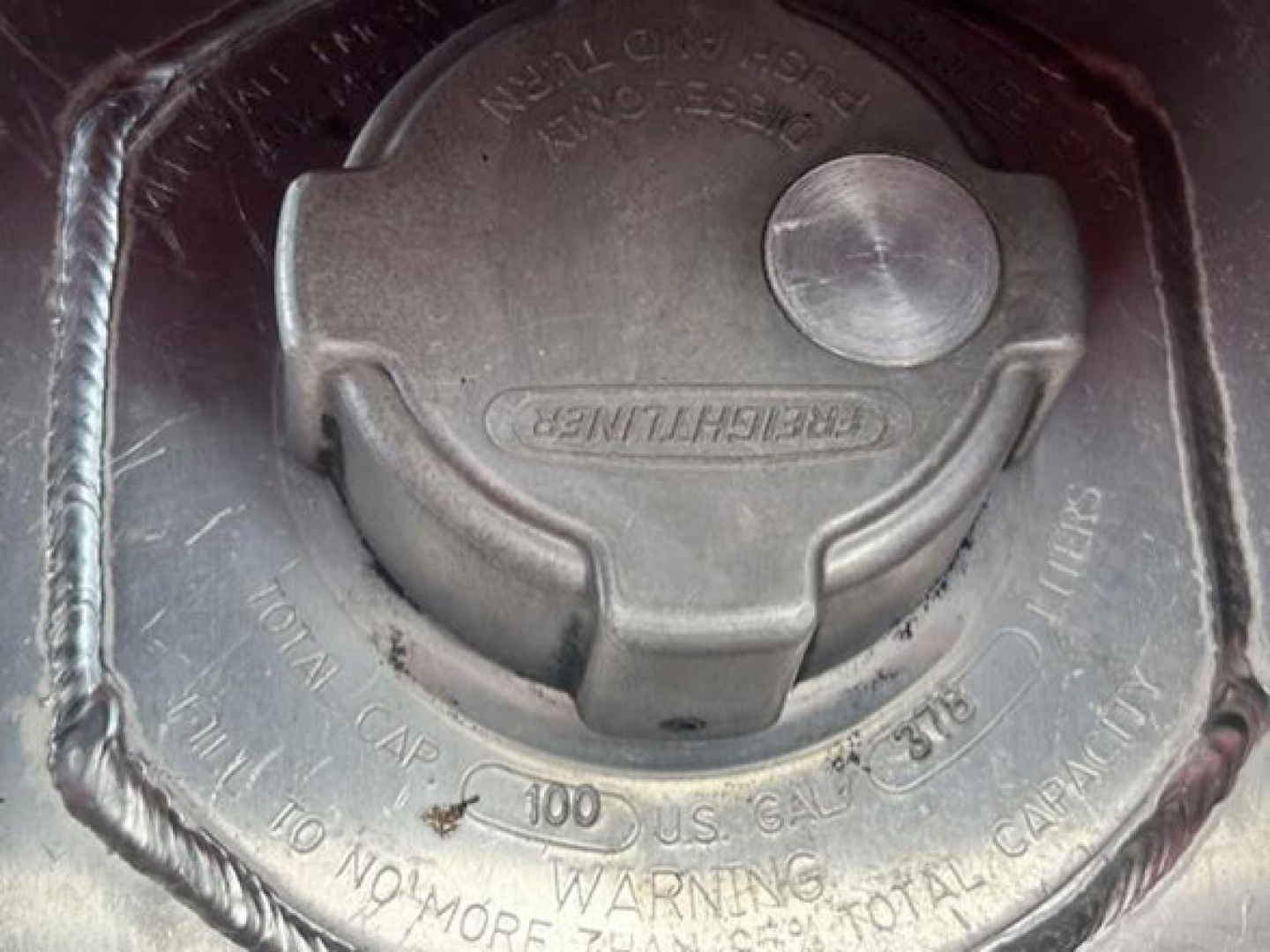 Fuel cap area of a Freightliner truck showing cap and surrounding surface with embossed text