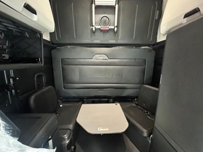 Cab interior of a Freightliner Cascadia 126 showing rear sleeper area with fold-out table and seating, black panels and storage compartments.