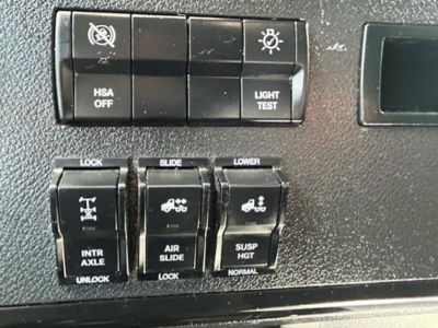 Dashboard switches showing HSA OFF, light test, lock/slide controls and air suspension indicators inside a Freightliner Cascadia truck cabin.