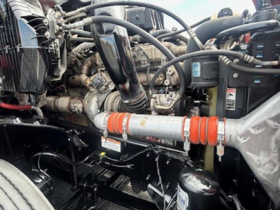 Front engine bay of a Freightliner Cascadia showing hoses, turbo, coolant reservoir, and orange hose with clamps.