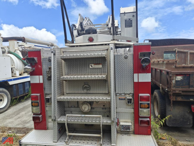Emergency One Quint fire truck rear with ladder rack and diverter compartments; metal diamond plate panels; writing panels and warning labels visible.
