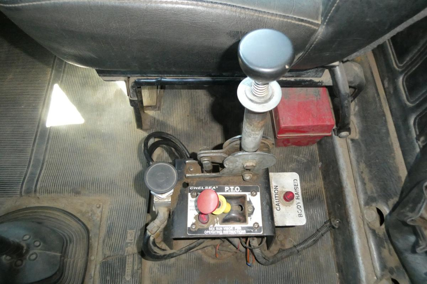 Truck interior showing gear shifter and control console with red start button and yellow knob, floor mat, and wiring harness in the cab of a Mack RD688S.