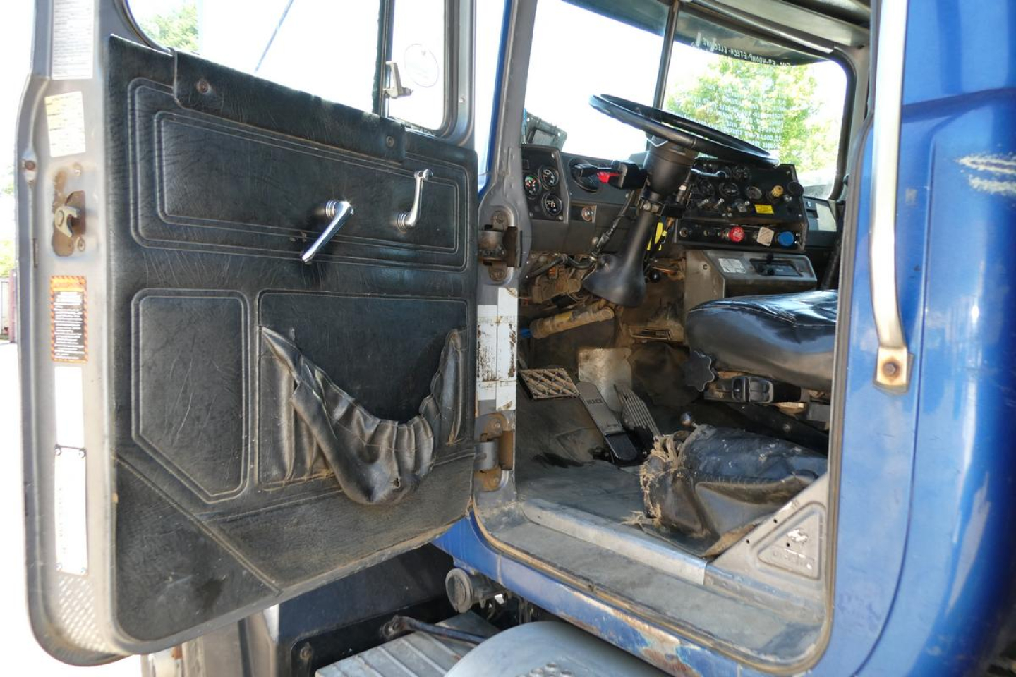 Cab interior of a 2000 Mack RD688S dump truck showing open driver door, steering wheel, dashboard, and pedals.