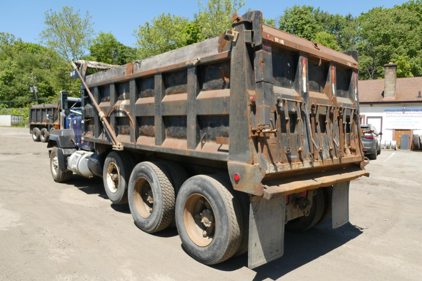 Dump truck rear three-quarter view showing open-top dump bed on a Mack RD688S with multiple axles and worn rust-colored metal side walls.