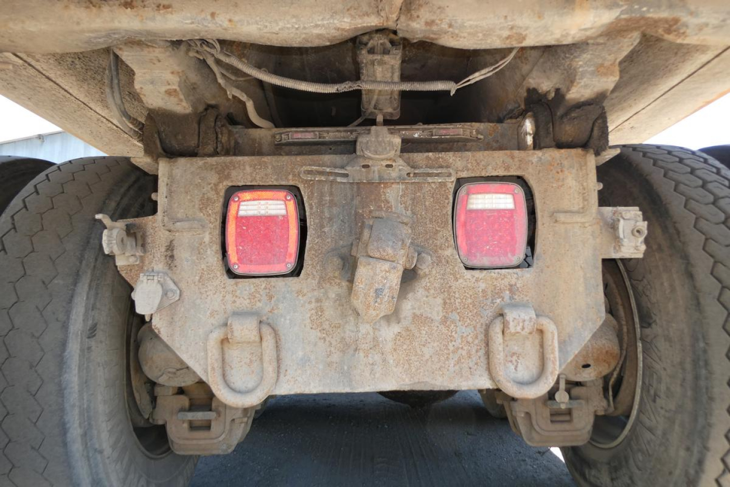 Rear view of a dump truck chassis showing tail lights, mud, and hitch assembly with visible mechanical components under the dump bed.