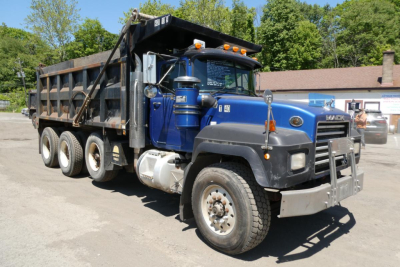 Dump truck cab and bed, blue Mack RD688S with dump bed open, front grille, large tires, and side mirrors visible.