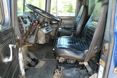 Truck interior of a 2000 Mack RD688S dump truck showing steering wheel, dashboard, and two front seats viewed from the driver’s side doorway.