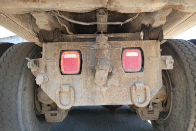 Rear view of a dump truck chassis showing tail lights, mud, and hitch assembly with visible mechanical components under the dump bed.