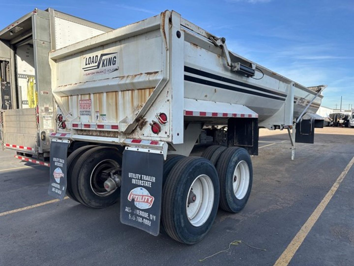 Load King frameless rock end dump trailer showing rear and side, with rust on body and dual rear axles.
