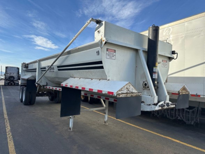 Load King frameless rock end dump trailer with hydraulic hoist, side rails, and support legs visible. Various warning labels on the body, number 19 on side.
