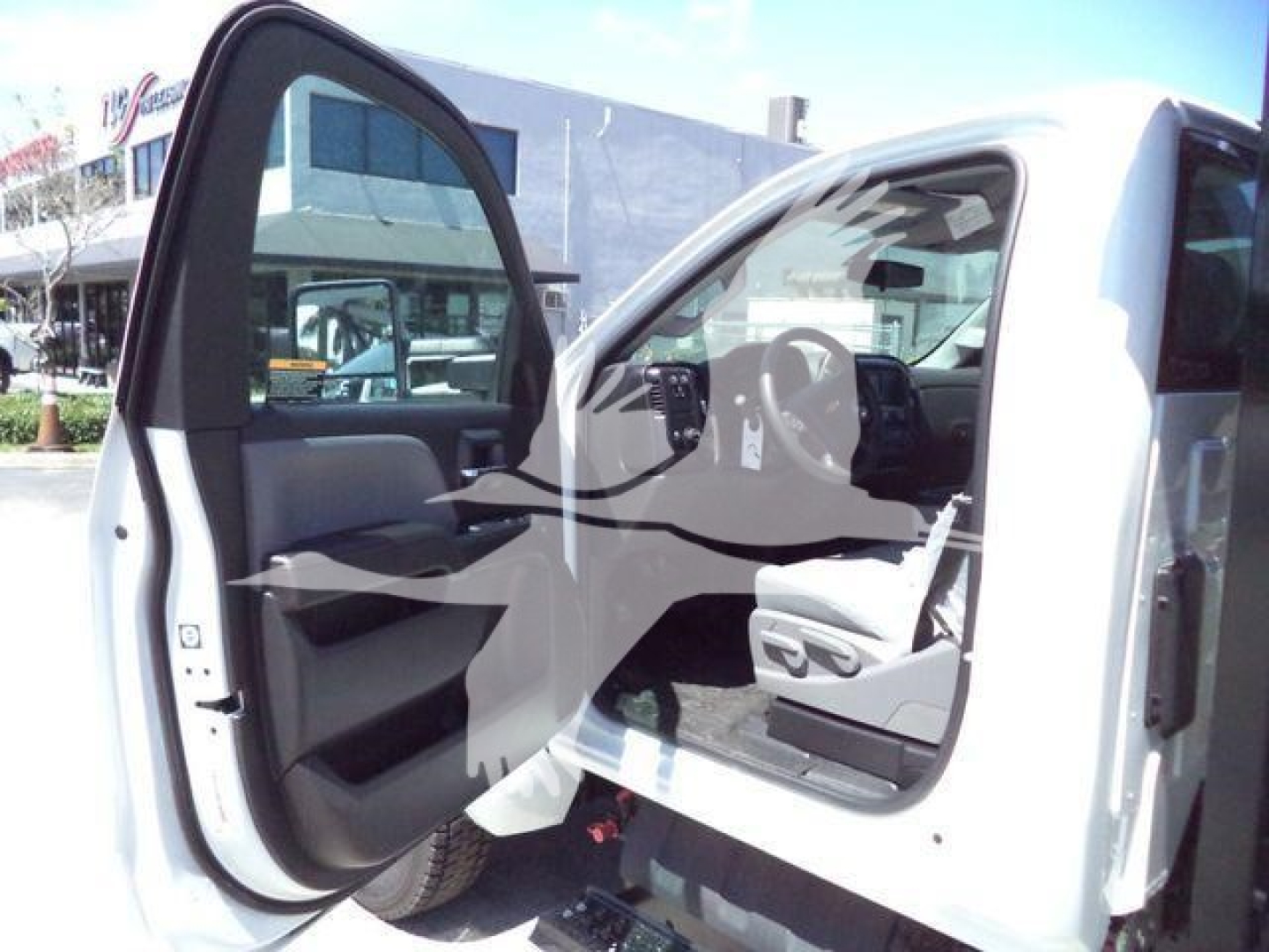 Truck cab interior visible with front door open showing driver seat and steering wheel of a 2023 Chevrolet Silverado 6500HD in a dealership setting.
