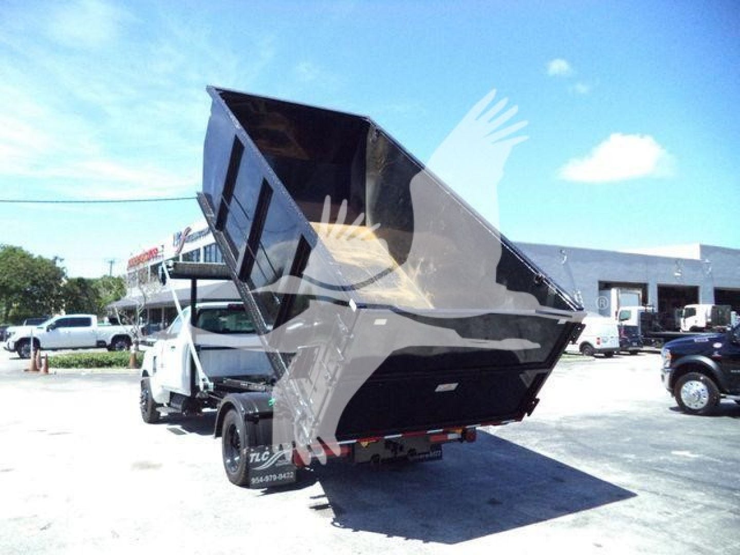 Truck bed of a 2023 Chevrolet Silverado 6500HD in raised dump position, a roll-off dump body on a flatbed tow truck lot.