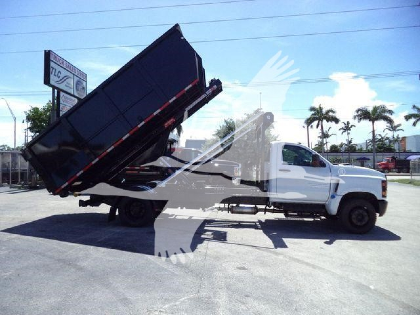 2023 Chevrolet Silverado 6500HD dump truck in raised bed tilt with white cab and black dump body in a lot, stock J05526FM, roll-off category.