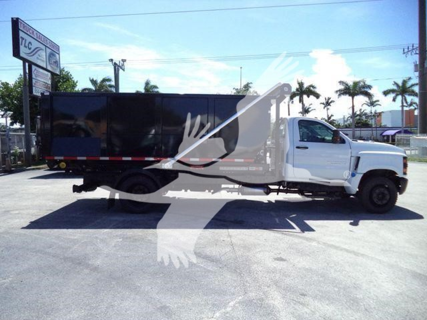 2023 Chevrolet Silverado 6500HD roll-off truck in dealership lot, side view showing cab and long black dump body with side rails.