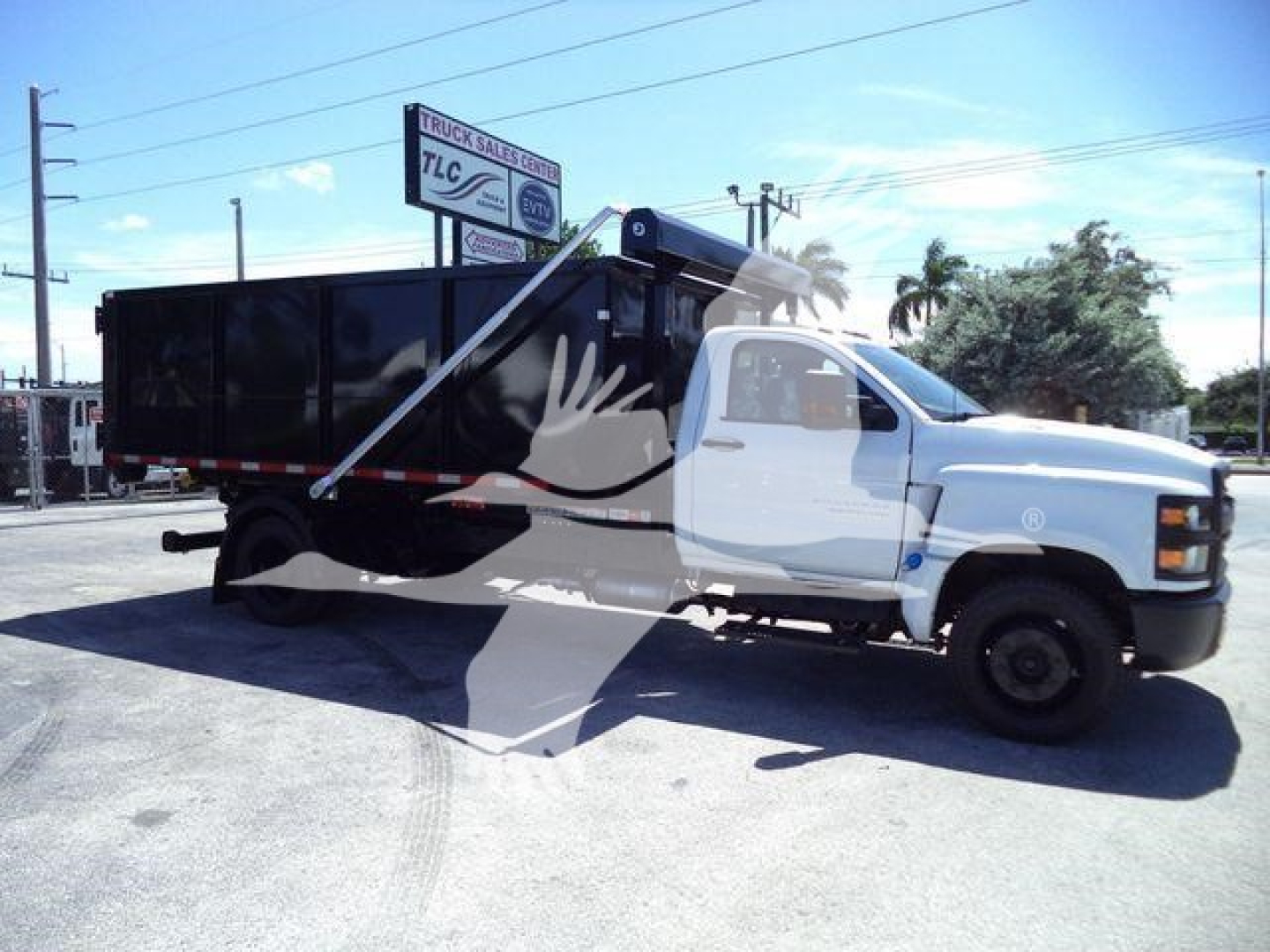 Truck bed with black dump body on a white Chevrolet Silverado 6500HD cab; roll-off truck in an outdoor lot.