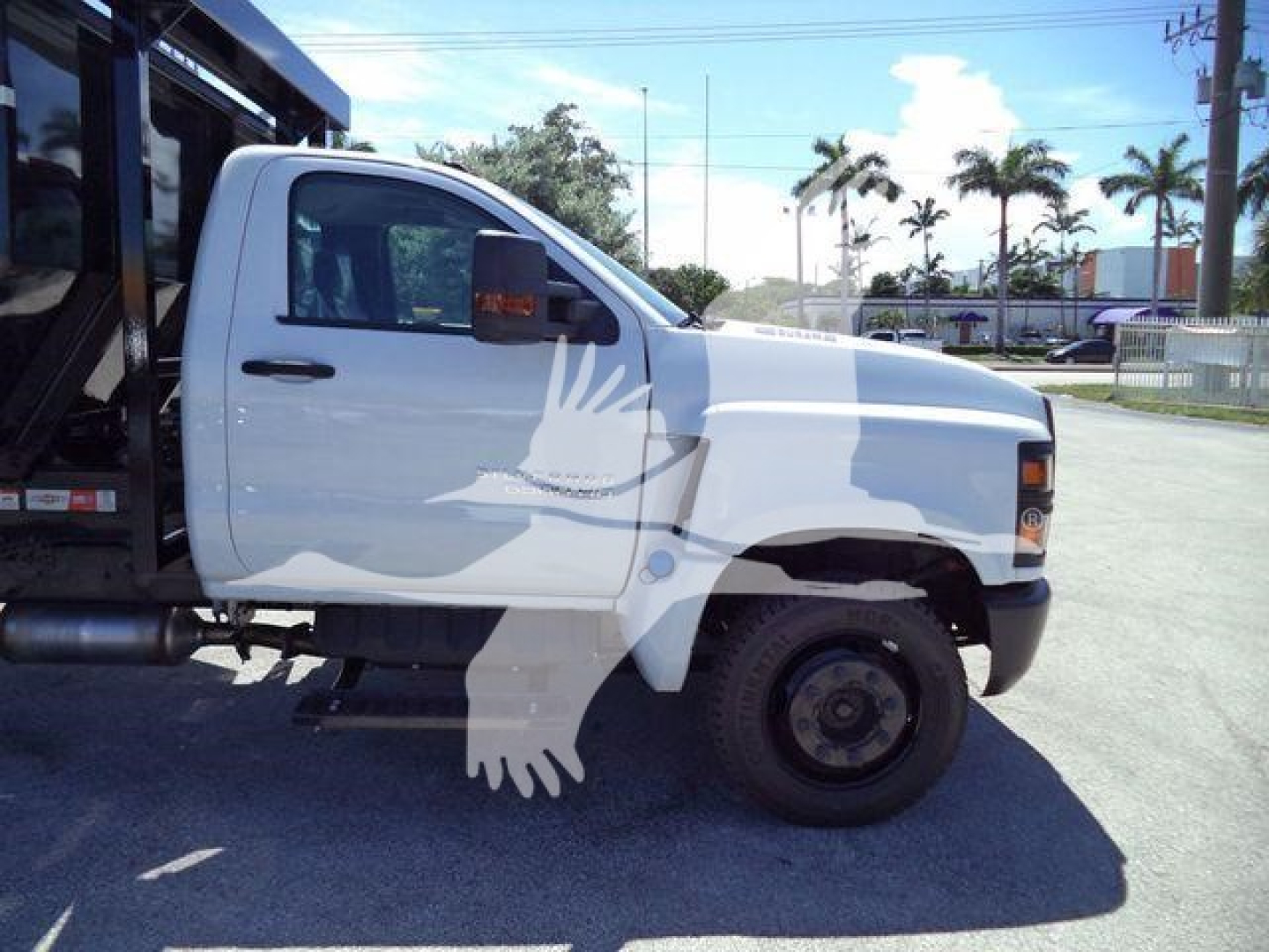 Truck side view showing white 2023 Chevrolet Silverado 6500HD roll-off truck with front wheel, steps, and graphic of a bird on door.