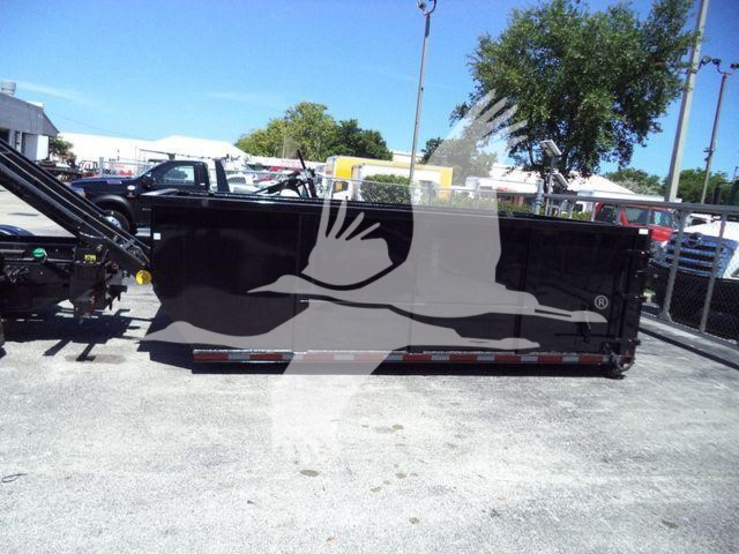 Truck bed/roll-off dumpster body with Chevrolet Silverado 6500HD in a dealership lot showing a black cargo container and surrounding equipment.