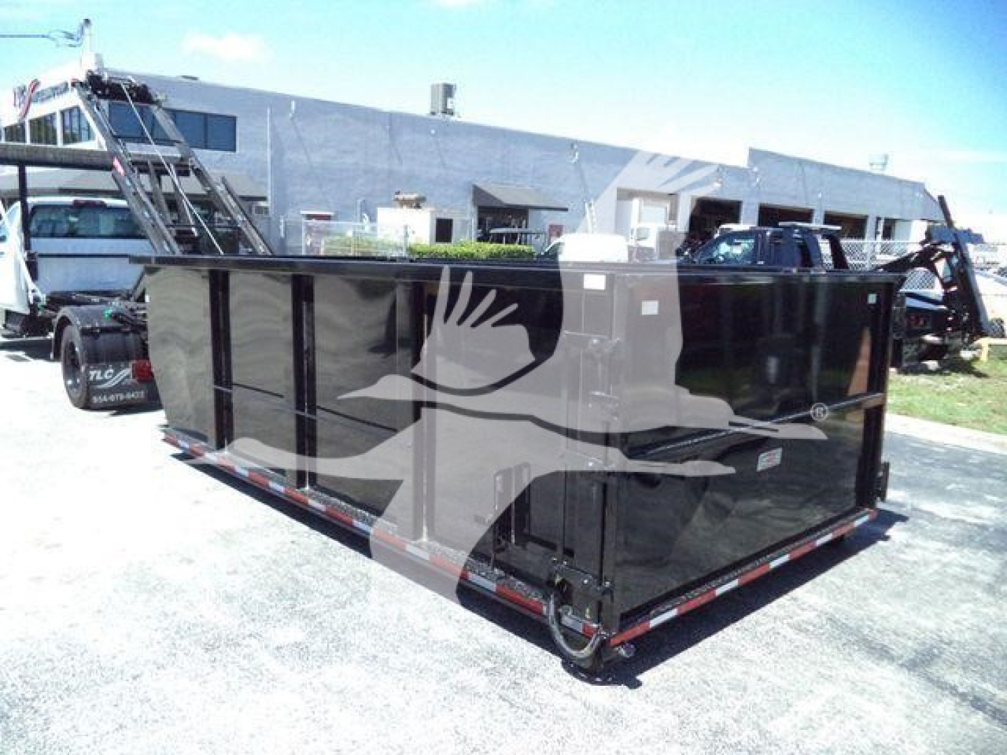 Rolloff truck dumpster in trailer with black painted exterior and reflective stripes showing on-site, with warehouse buildings in background.