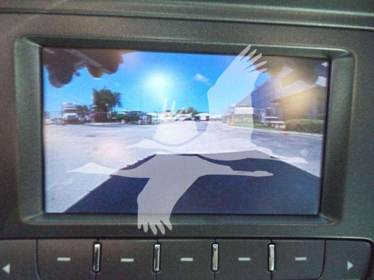 Truck rearview camera display showing a parking lot with blue sky and vehicles in the distance.