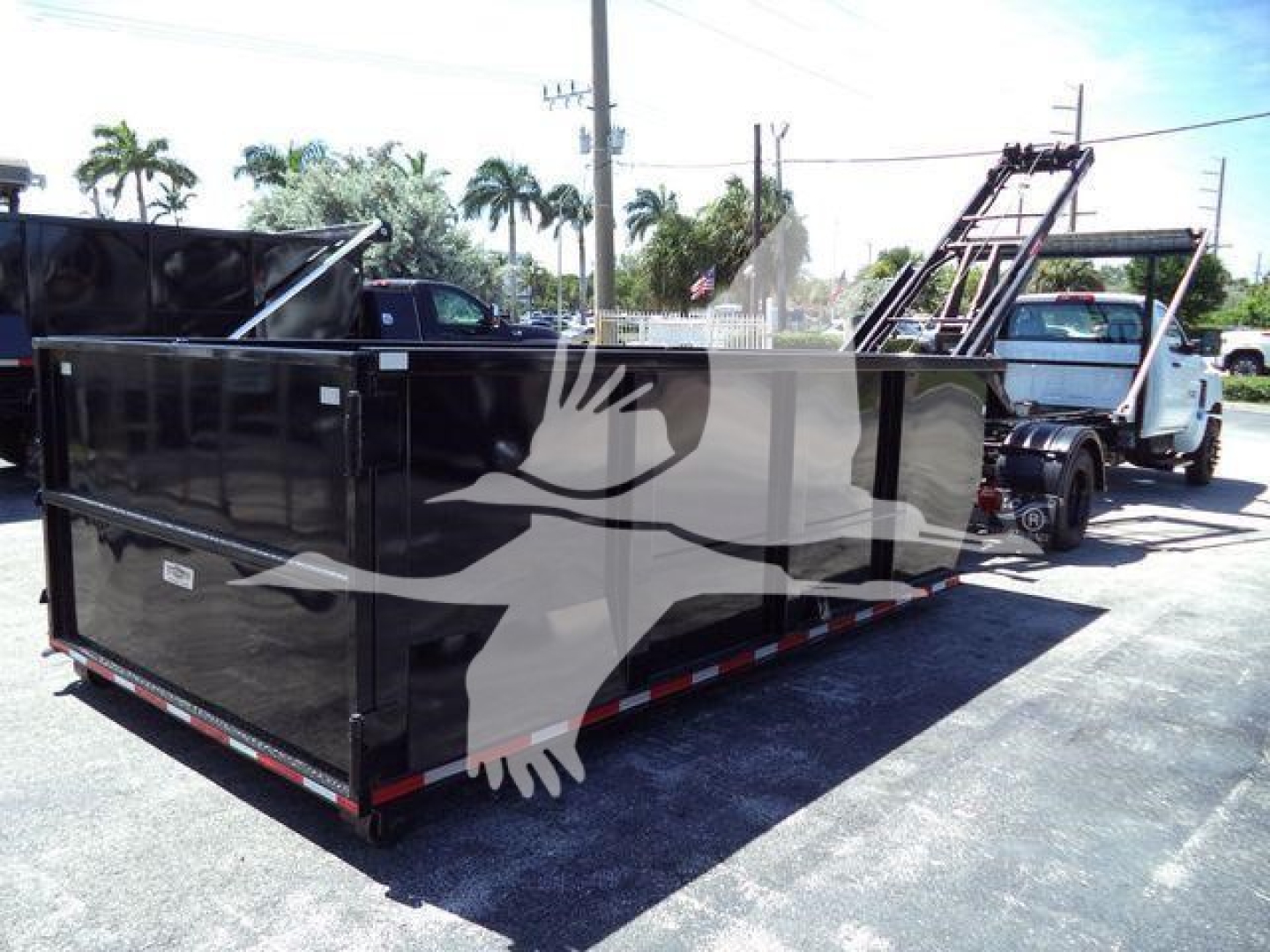 Truck bed with large black roll-off dumpster attached to a Silverado 6500HD in a lot.