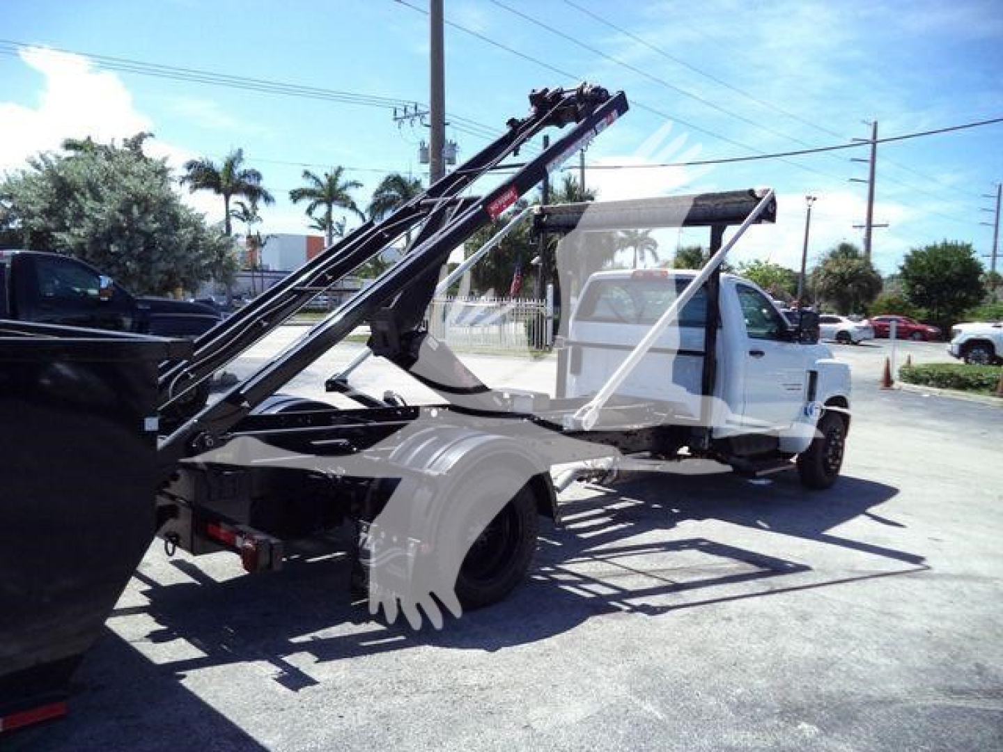 Truck bed with hydraulic rolloff hoist on a white 2023 Chevrolet Silverado 6500HD, side view showing equipment and hydraulic arms.
