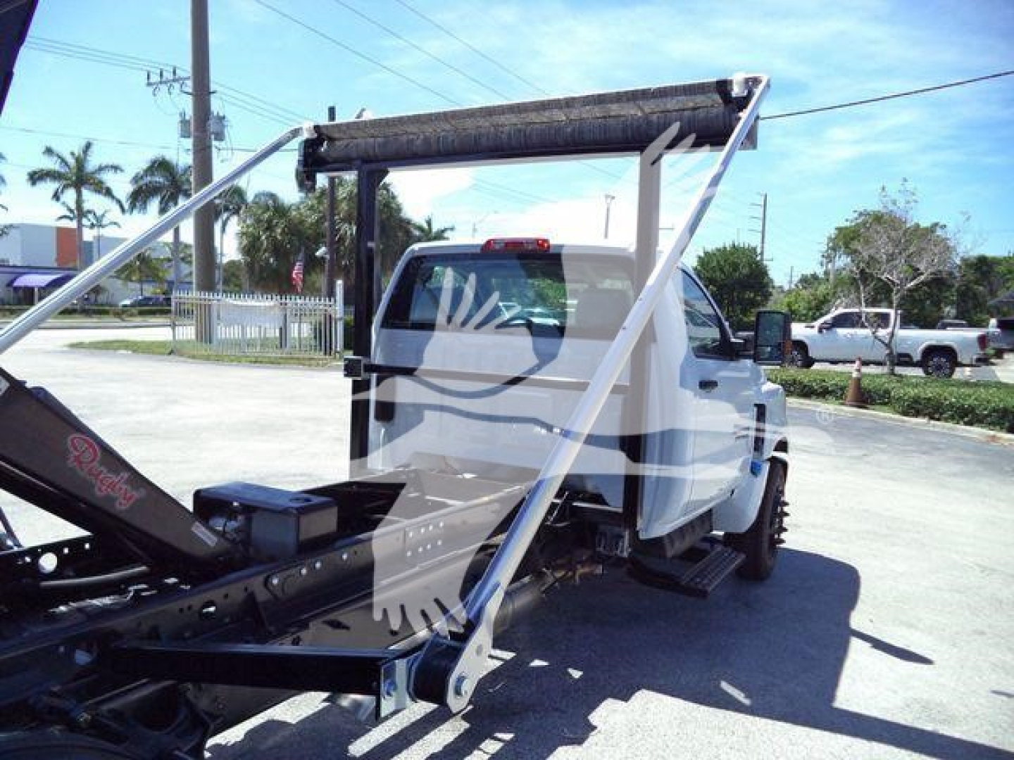 Tow truck with roll-off system on a white Chevrolet Silverado 6500HD cab; rear chassis and hydraulic components visible.