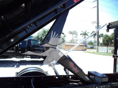 Truck bed hydraulics of a 2023 Chevrolet Silverado 6500HD roll-off tilt showing hydraulic arm with 'Roughneck' branding and part of wheel and truck frame.