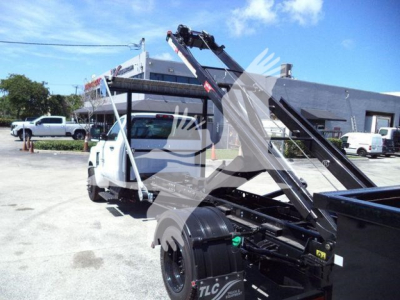 Truck chassis and hydraulic arm lift attached to a white Chevrolet Silverado 6500HD roll-off truck in a dealership lot.