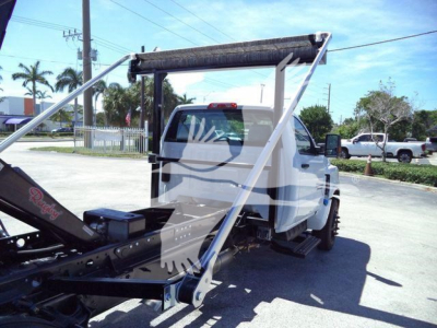 Tow truck with roll-off system on a white Chevrolet Silverado 6500HD cab; rear chassis and hydraulic components visible.