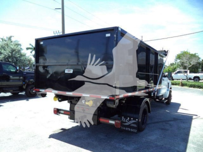 Truck rear view showing dump bed with black/dark container and white Chevrolet Silverado 6500HD, no plate, side view mirrors, dual rear wheels.