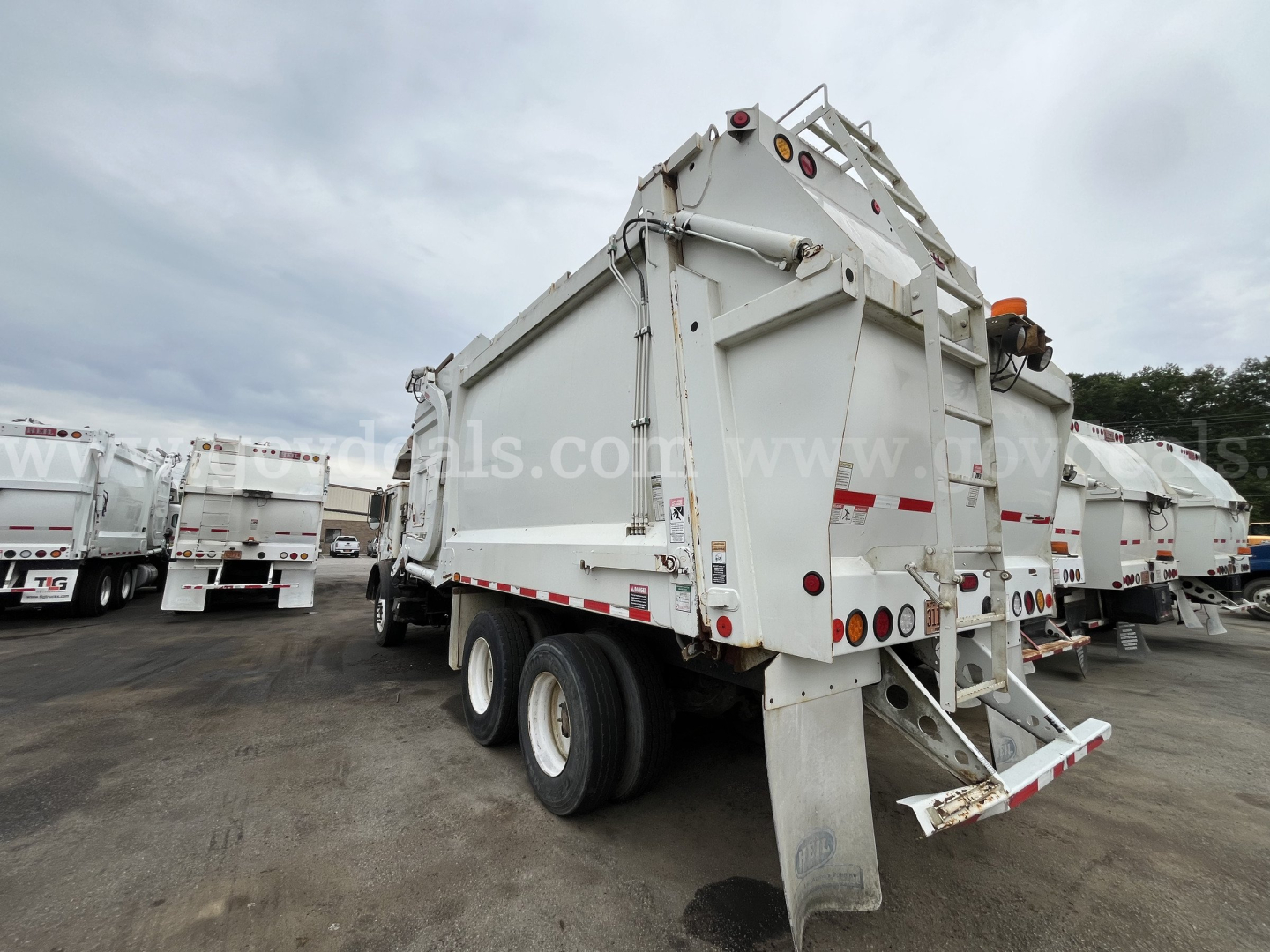Rear view of a white Mack MRU613 dump truck in a used truck lot showing dual rear wheels and tailgate.