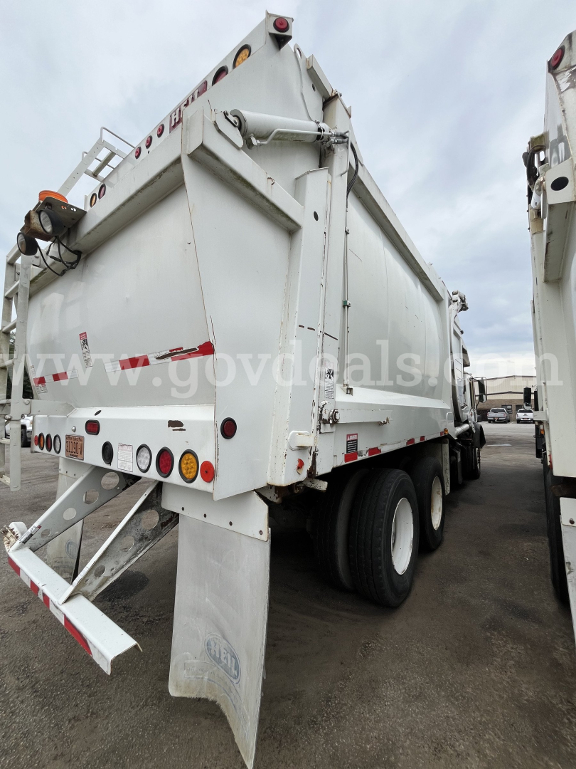 Rear view of a white Mack MRU613 dump truck in service showing dual rear wheels and tailgate with red and amber marker lights.