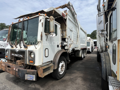 Dump truck in service bay showing Mack MRU613 front cab and dumping body with hydraulic arm, white with rust accents and license plate area.