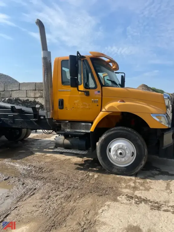 Dump truck side view showing tall exhaust, yellow cab with black steps, and chrome wheel hub; no body on dump bed.