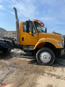 Dump truck side view showing tall exhaust, yellow cab with black steps, and chrome wheel hub; no body on dump bed.