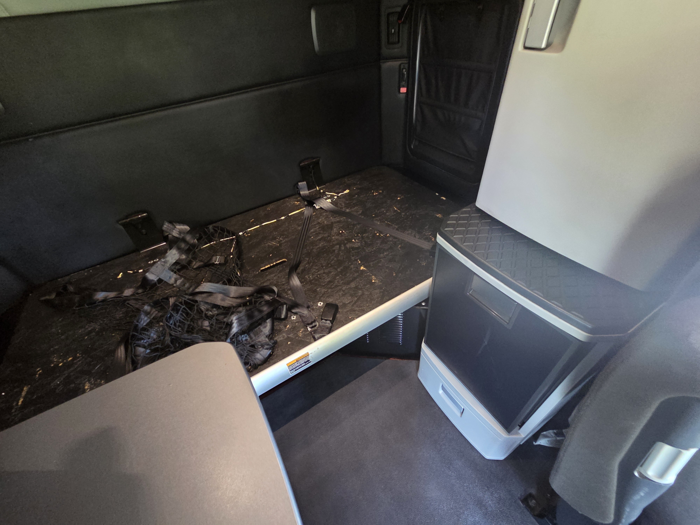 Truck cab interior of a Kenworth T680 with debris on the floor, a collapsible bunk bed rail, and a heater/console unit visible.