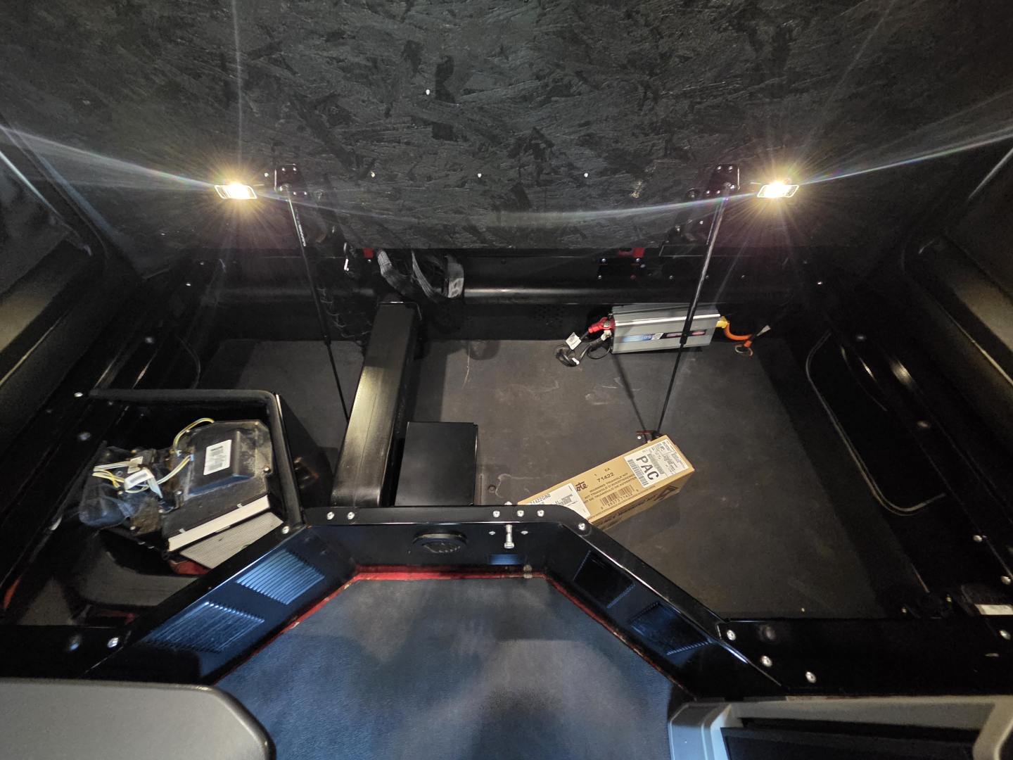 Kenworth T680 cab interior view showing under-dash components and storage area; wiring harnesses and a cardboard box visible.