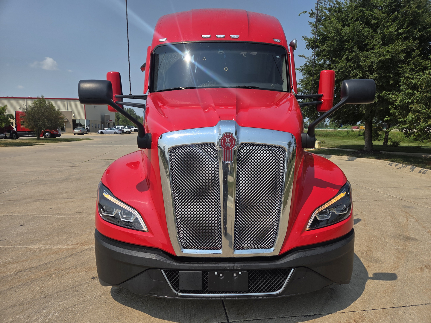 Kenworth T680 front view showing large chrome grille, red cab, and black bumper; headlights visible.