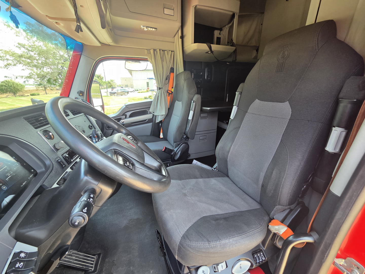 Kenworth T680 interior showing driver seat and steering wheel with dashboard, cab area, and sleeper in background.