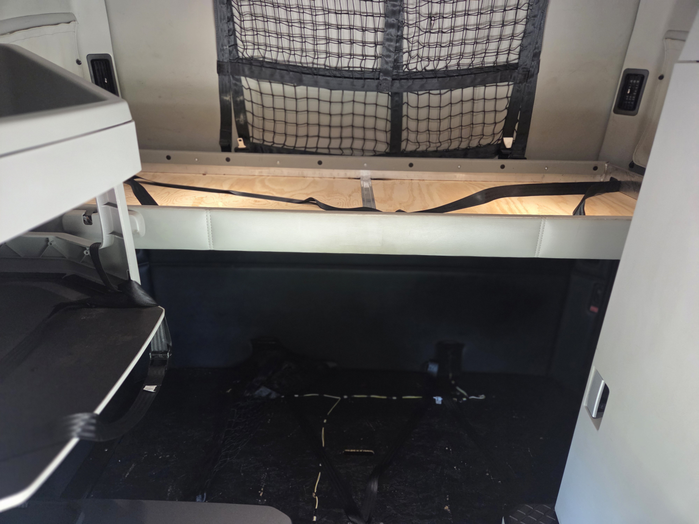 Kenworth T680 sleeper cab interior with storage area and netted bulkhead, cargo space visible, dashboard area on left.