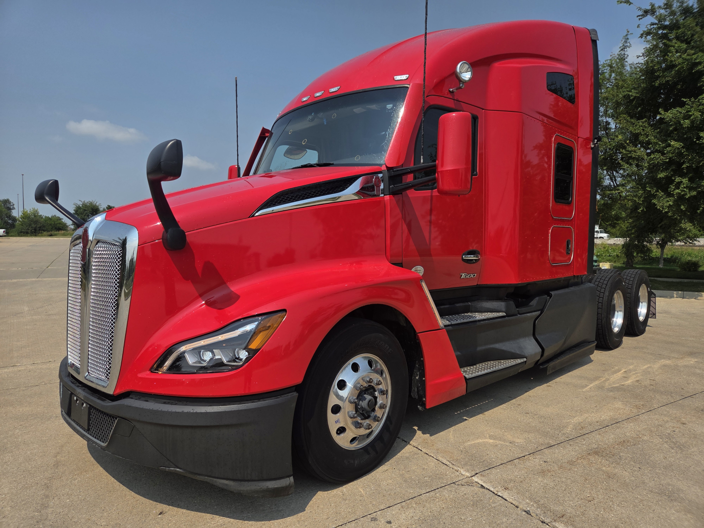 Red Kenworth T680 tractor side view showing cab, front grille, headlights, and dual rear axles with chrome wheels.