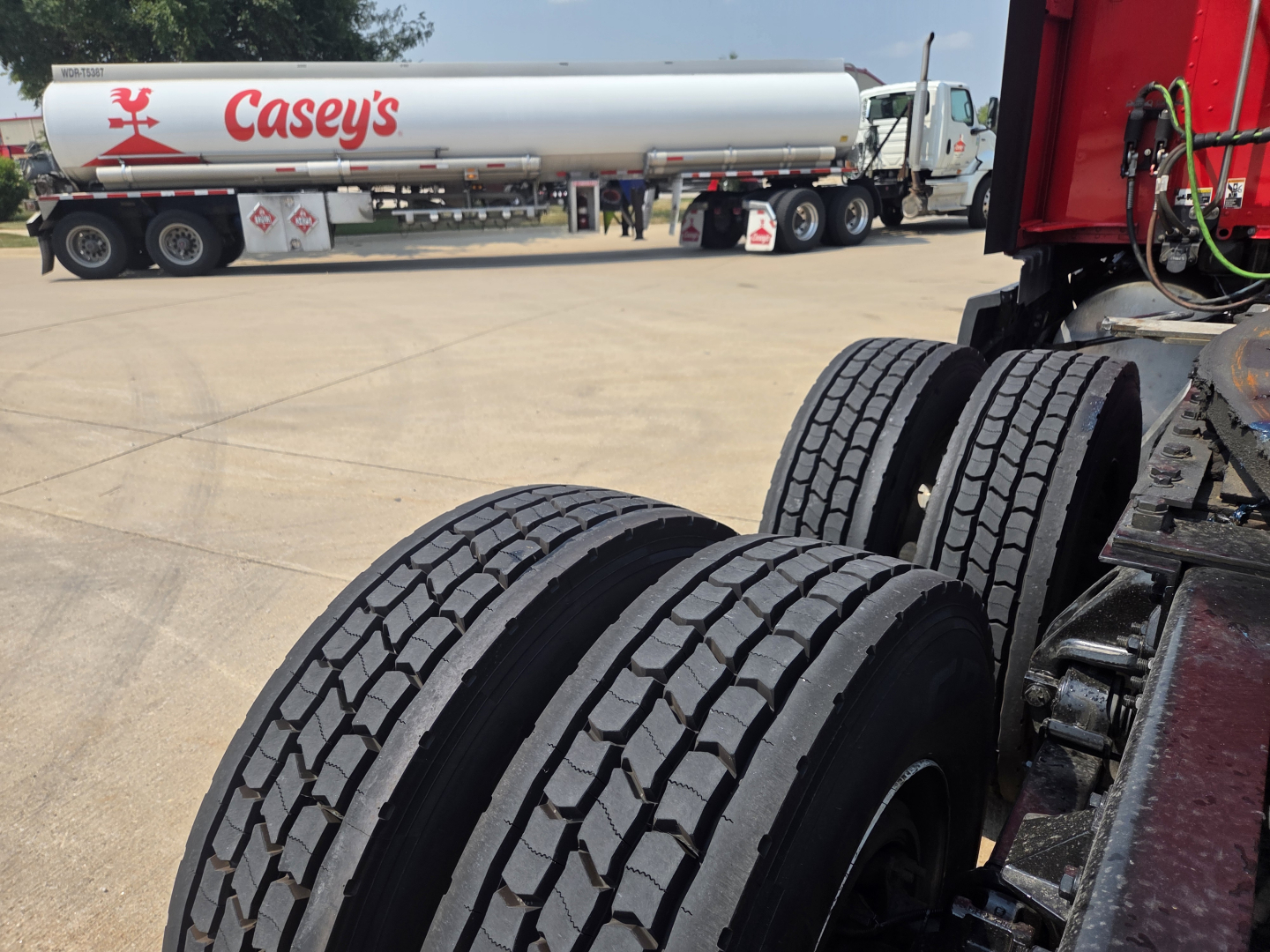Kenworth T680 truck in a dealership lot with a Caseys fuel tanker trailer in background; dual rear tires visible and part of the tractor unit on the right.