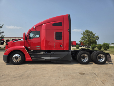 Kenworth T680 tractor cab side view showing red exterior, door with window, fuel/equipment compartments, and triple rear axles with chrome wheels.